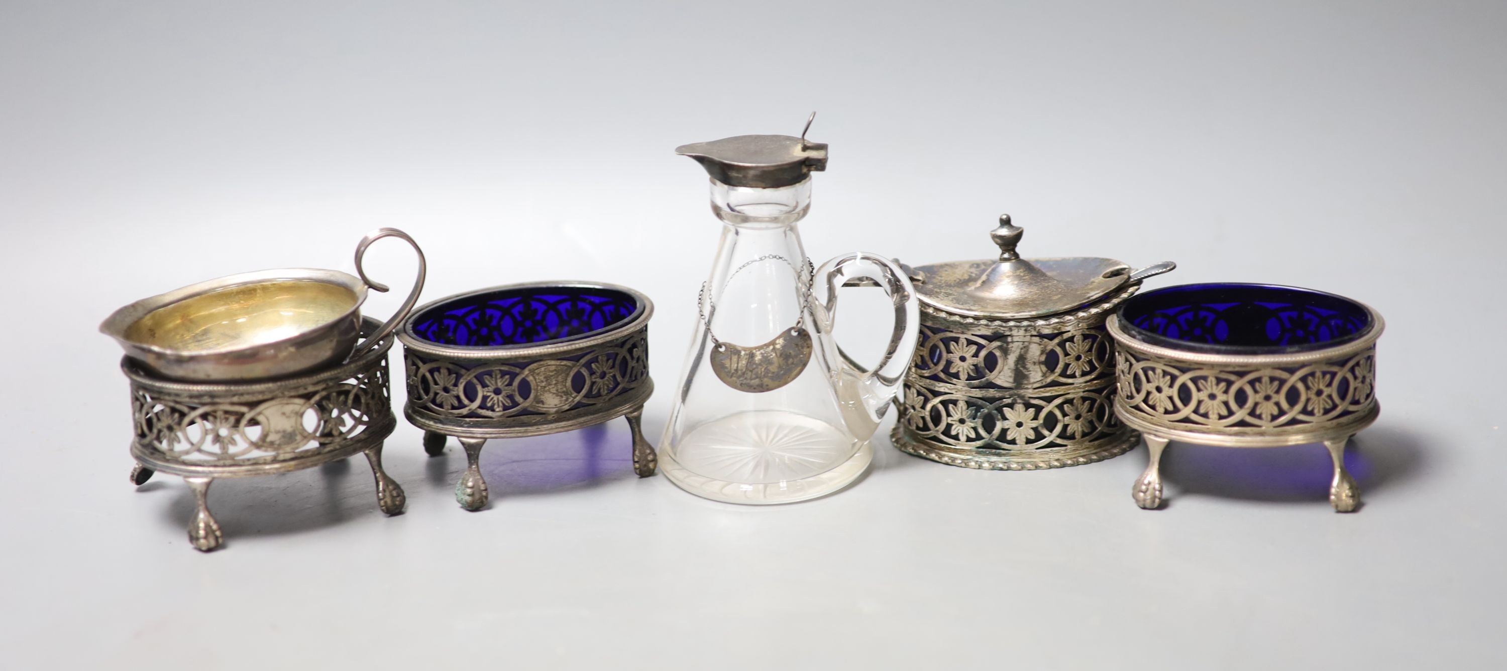 An Edwardian pierced silver oval mustard pot, with liner, a set of three similar salts, one lacking liner, a silver mounted glass whisky tot jug and a small continental jug.